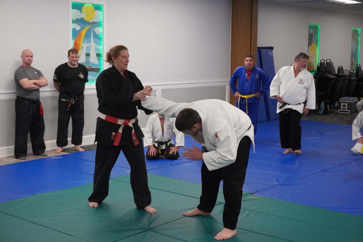 Sensei Debbie Burk (left, center) demonstrating a wrist technique on David Racine Jr (right, center).