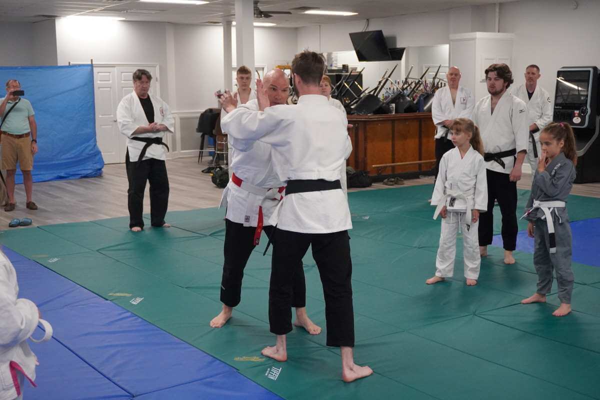 Sensei Mike Hickey (Left behind center) talking about a neck sweep with his partner Zion Coldiron (front center right), particularly about hand placement.